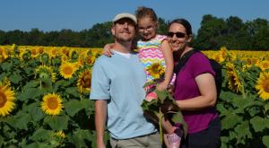 A man with dark glasses holding his young daughter on his hip with his wife holding onto the both of them.